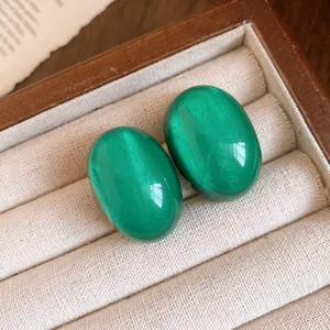 Close-up of green resin oval stud earrings with a cat-eye effect in a jewelry box