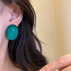 Detailed close-up view of a stylish oval teal resin stud earring on a model's ear