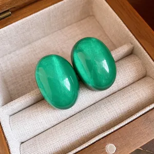 Close-up of green oval resin stud earrings with a velvet-like cat-eye sheen
