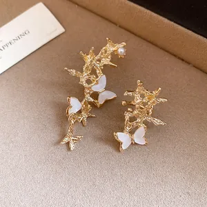 Close-up detail of gold asymmetric branch ear cuffs with white shell butterfly elements