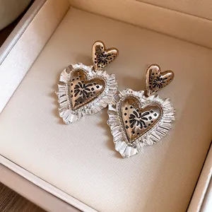 Dettaglio macro di orecchini a cuore vintage con bordi in argento plissettato e motivi