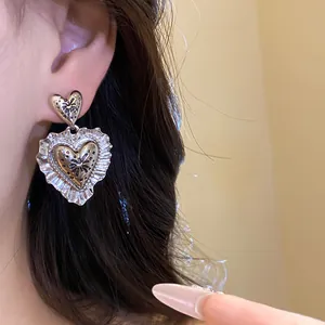 Dettaglio di orecchini pendenti a cuore pieghettato in stile vintage e agoceleste.
