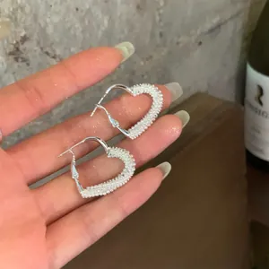 Elegant heart-shaped hoop earrings in silver finish with delicate white seed pearls.