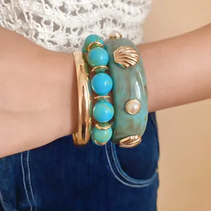 Close-up of stylish teal resin bangle with gold shell motifs and turquoise beaded bracelet