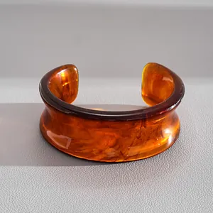 Dettaglio di un ampio bracciale a polsino in acrilico ambra marmorizzato trasparente.