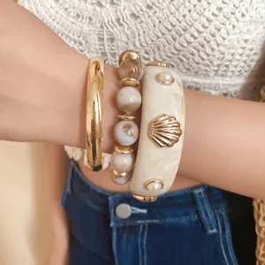 Detailed view of stacked bracelets featuring a gold shell resin bangle and marbled stone beads