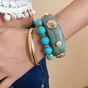 Detailed view of marbled resin bangle with gold shell charms and turquoise bead bracelet.