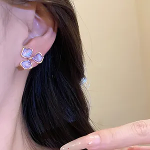 Detailansicht eines lila Blumen-Emaille-Ohrrings mit Goldrand am Ohr eines Models.