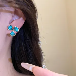 Detailansicht eines blauen Emaille-Blumenohrrings am Ohr mit hochwertiger Textur