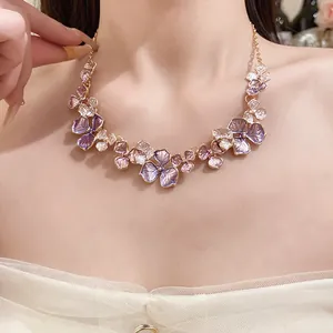 Detailansicht einer eleganten Halskette mit lila Emaille-Blumen am Halsausschnitt.