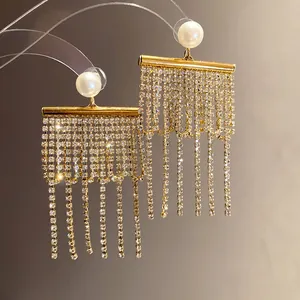 Détail de boucles d'oreilles dorées élégantes avec perles et franges de strass.