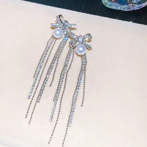 Detail of sparkling bow earrings with long rhinestone tassels and central pearl studs.
