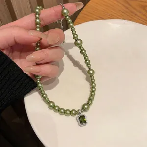 Elegant green pearl necklace with square zircon pendant held over white plate.