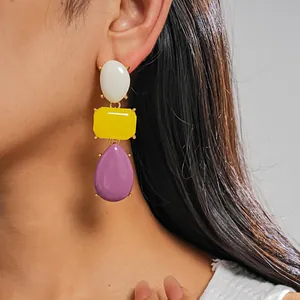 Dettaglio di orecchini pendenti geometrici in resina colorata indossati dal modello