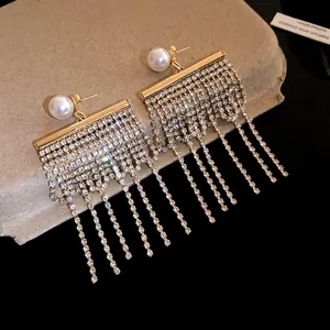 Gros plan de boucles d'oreilles dorées élégantes avec perles blanches et longs glands.