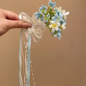 Detail view of a forest-style flower hair clip with light blue petals and ribbons.