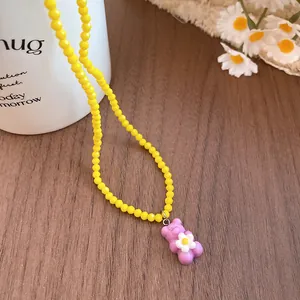 Macro detail of yellow beaded necklace with purple resin bear pendant and white flower