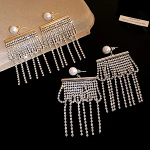 Détail de boucles d'oreilles à pompons en strass avec perles blanches sur fond noir