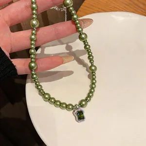 Detailed view of green rectangular zircon pendant and olive green pearl beads necklace