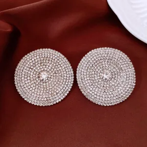 Dettaglio ravvicinato di orecchini a lobo circolari con pavé di strass su tessuto bordeaux.