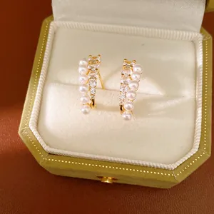 Elegant pearl and zircon curved stud earrings displayed in a luxury green velvet jewelry box