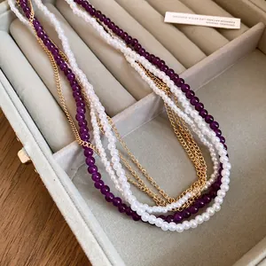 Elegant multi-layer necklace with white pearls, purple beads and gold chains in a jewelry box.