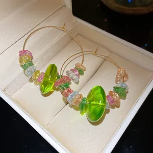 Nahaufnahme von bunten Glasperlen und Natursteinen an goldfarbenen Creolen für Damen