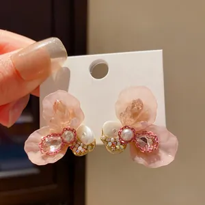 Close-up of elegant resin flower stud earrings with pearl and rhinestone center detailing.