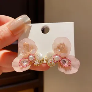 Close-up view of elegant pink resin flower stud earrings with pearls and shiny rhinestones