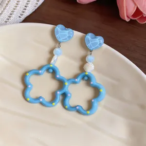 Primer plano de pendientes de corazón azul con detalle de concha y aros festoneados