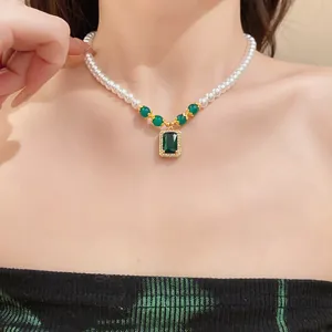 Detail view of a vintage pearl necklace with a square emerald-green zircon pendant on a model.