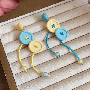 Primer plano de pendientes largos con forma de botón en azul y amarillo vibrante.