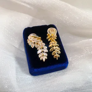 Close-up view of gold-plated leaf ear clips with sparkling cubic zirconia on blue velvet