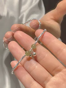 Close-up of a silver bamboo-joint bracelet featuring green beads and small bells, held by hand.