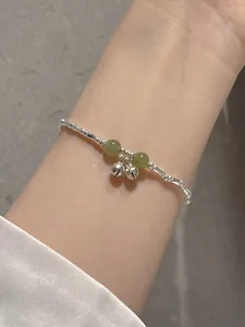Close-up detail of a silver bamboo-style bracelet with green beads and charming small bells
