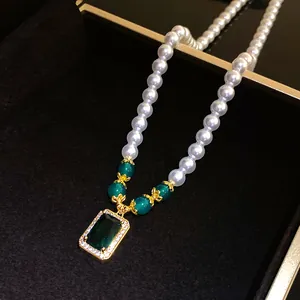 Close-up of vintage pearl necklace with emerald green square pendant in a jewelry box