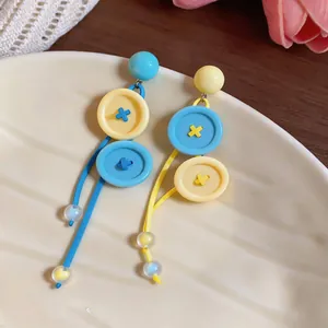Vista detallada de pendientes coloridos estilo dopamina con colgantes de botones amarillos.