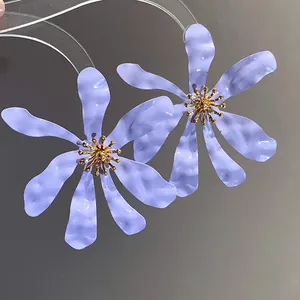 Close-up of oversized purple flower earrings with gold stamens in a vacation style.