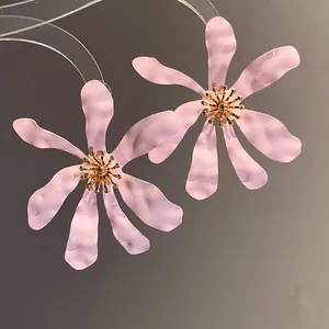Close-up of oversized pink flower earrings with golden stamen and textured petals