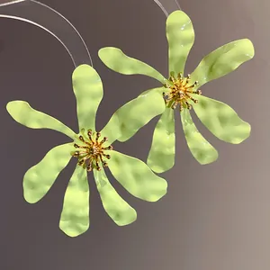 Close-up of exaggerated lime green flower earrings featuring textured petals and golden centers