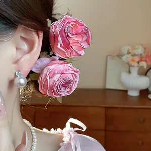 Dettaglio di forcine per capelli a forma di rosa in tessuto rosa indossate dal modello.