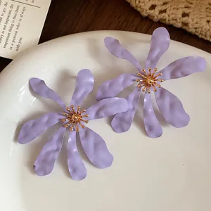 Detailed view of exaggerated purple floral earrings featuring textured petals and a gold core.