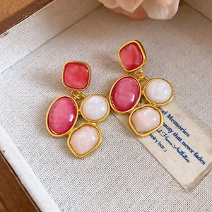 Dettaglio di orecchini vintage in resina con pietre rosa e bianche in castone dorato.