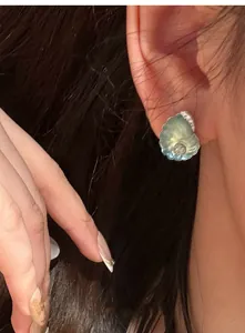 Detailansicht eines eleganten blauen Harz-Ohrsteckers in Muschelform am Ohr.