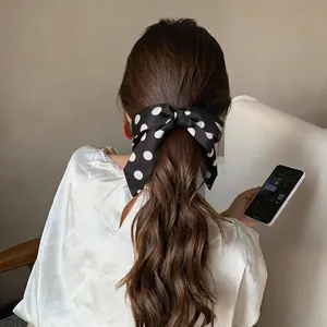 Detailed view of a black and white polka dot satin bow scrunchie in a ponytail