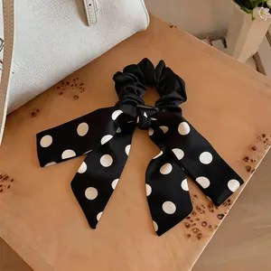 Detail view of the elegant black and white polka dot satin scrunchie with a long ribbon bow.