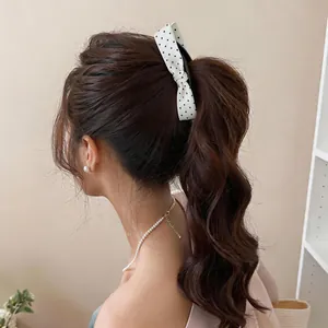 Close-up of a white polka dot bow scrunchie securing a high wavy ponytail