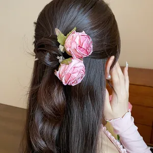 Dettaglio di forcine per capelli con rose in tessuto rosa su un'acconciatura mossa.