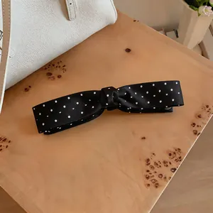 Close-up of an elegant black satin bow hair clip featuring classic white polka dots design