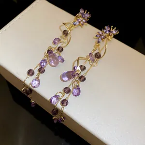 Detailed close-up of elegant purple crystal butterfly tassel earrings on a white display box